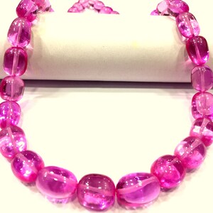 Peut inclure: Un collier composé de perles ovales roses, transparentes et légèrement brillantes.