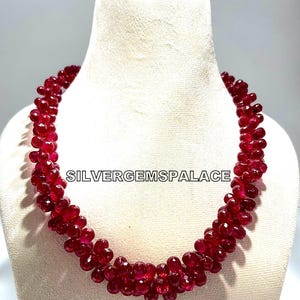 May include: A red ruby gemstone necklace with faceted beads. The necklace is displayed on a white mannequin bust. The text "SILVERGEMSPALACE" is visible on the necklace.