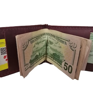 Könnte beinhalten: Eine dunkelrote Ledergeldbörse mit einem Geldclip, in dem sich mehrere 50-Euro-Scheine befinden. Die Geldbörse hat auf der linken Seite einen Steckplatz für eine Karte.