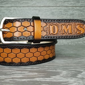 May include: A brown leather belt with a honeycomb pattern and a silver buckle. The belt has a dark brown border and the initials "DMS" are embossed on the tip.