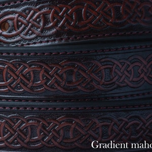 Könnte beinhalten: Nahaufnahme von mehreren Ledergürteln mit einem Farbverlauf in Mahagoni. Die Gürtel weisen ein geprägtes keltisches Knotenmuster auf und sind mit bordeauxrotem Faden genäht. Der Text "Gradient mahogany" ist unten sichtbar.