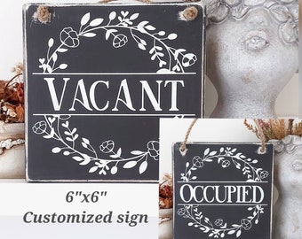 May include: Two 15.24 cm x 15.24 cm wooden signs with a black background and white floral wreaths. The top sign says "VACANT" and the bottom sign says "OCCUPIED".