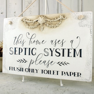 May include: White sign with distressed paint and a decorative floral design at the top. The sign reads "This home uses a SEPTIC SYSTEM please FLUSH ONLY TOILET PAPER".