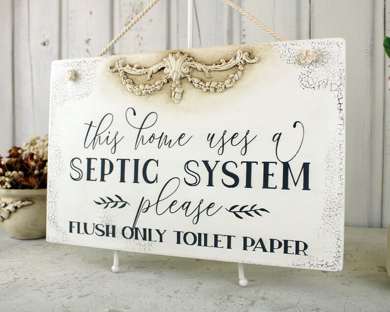 May include: White sign with distressed paint and a decorative floral design at the top. The sign reads "This home uses a SEPTIC SYSTEM please FLUSH ONLY TOILET PAPER".
