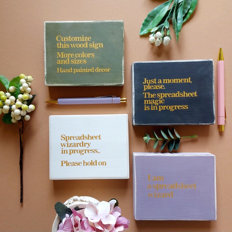 Wooden signs with gold lettering on different colored backgrounds. The signs say "Customize this wood sign More colors and sizes Hand painted decor", "Just a moment, please. The spreadsheet magic is in progress", "Spreadsheet wizardry in progress... Please hold on", and "I am a spreadsheet wizard".