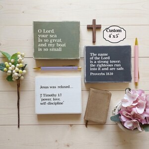 May include: Three rectangular wooden signs with white text: one olive green reading O Lord, your sea is so great, and my boat is so small; one black reading The name of the Lord is a strong tower; one white reading Jesus was relaxed... 2 Timothy 1:7.