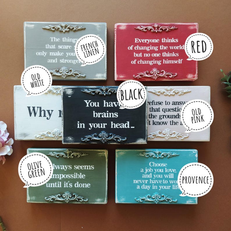 May include: A collection of rectangular wooden signs in various colors, including gray, red, black, white, green, and blue. Each sign features a quote in white lettering and ornate decorative trim.