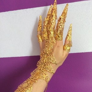 May include: Gold filigree finger rings and bracelet with intricate designs. The rings are long and pointed, resembling claws.