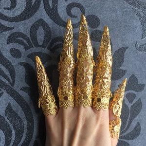 May include: Set of six gold-tone finger rings with intricate filigree designs. The rings are designed to be worn on each finger, extending beyond the fingertip.