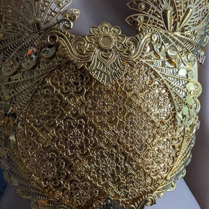 May include: A gold-colored metal bodice with intricate floral and peacock-inspired designs. The bodice is made of delicate, filigree-like metalwork.
