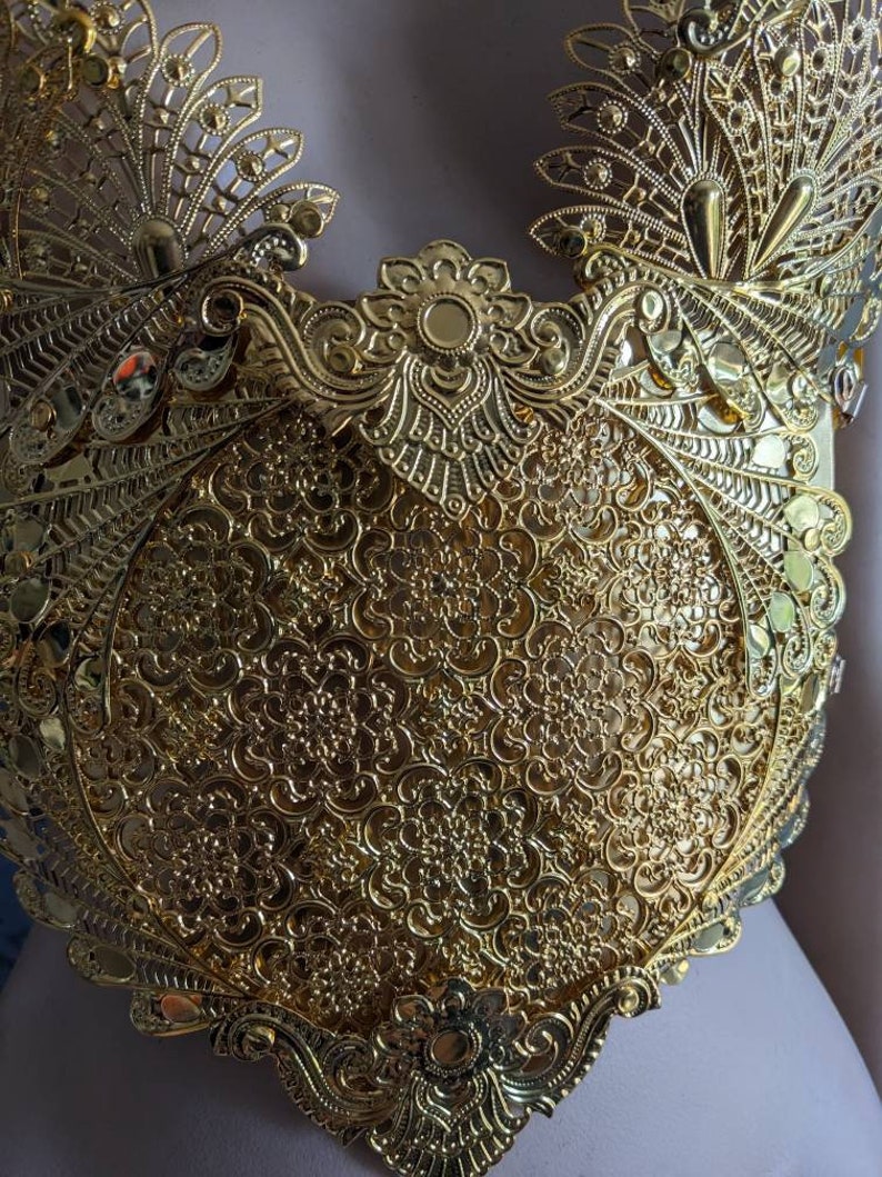 May include: A gold-colored metal bodice with intricate floral and peacock-inspired designs. The bodice is made of delicate, filigree-like metalwork.