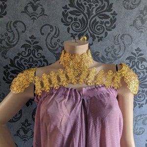 May include: A gold-colored, intricate, lacy, decorative shoulder piece and choker necklace. The shoulder piece is designed to be worn on both shoulders and is connected to the choker necklace.