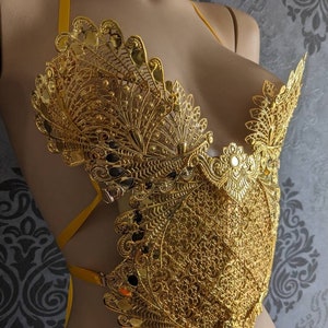 May include: A gold-colored, intricate, and detailed, decorative,  halter-style top with a delicate, lacy design. The top is made of metal and has a  peacock-like pattern.