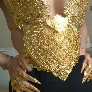 May include: A gold-colored, ornate, decorative bodice with a detailed, intricate design. The bodice is made of metal and has a delicate, feminine look.