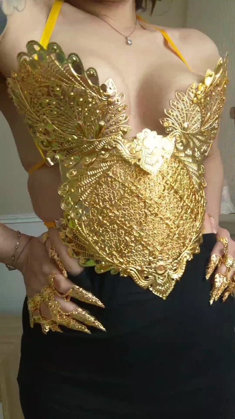 May include: A gold-colored, ornate, decorative bodice with a detailed, intricate design. The bodice is made of metal and has a delicate, feminine look.