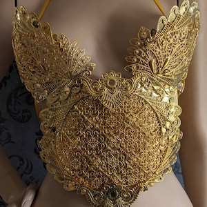 May include: A gold-colored, ornate, decorative piece of jewelry with a delicate, intricate design. The piece is shaped like a heart and has a floral pattern.