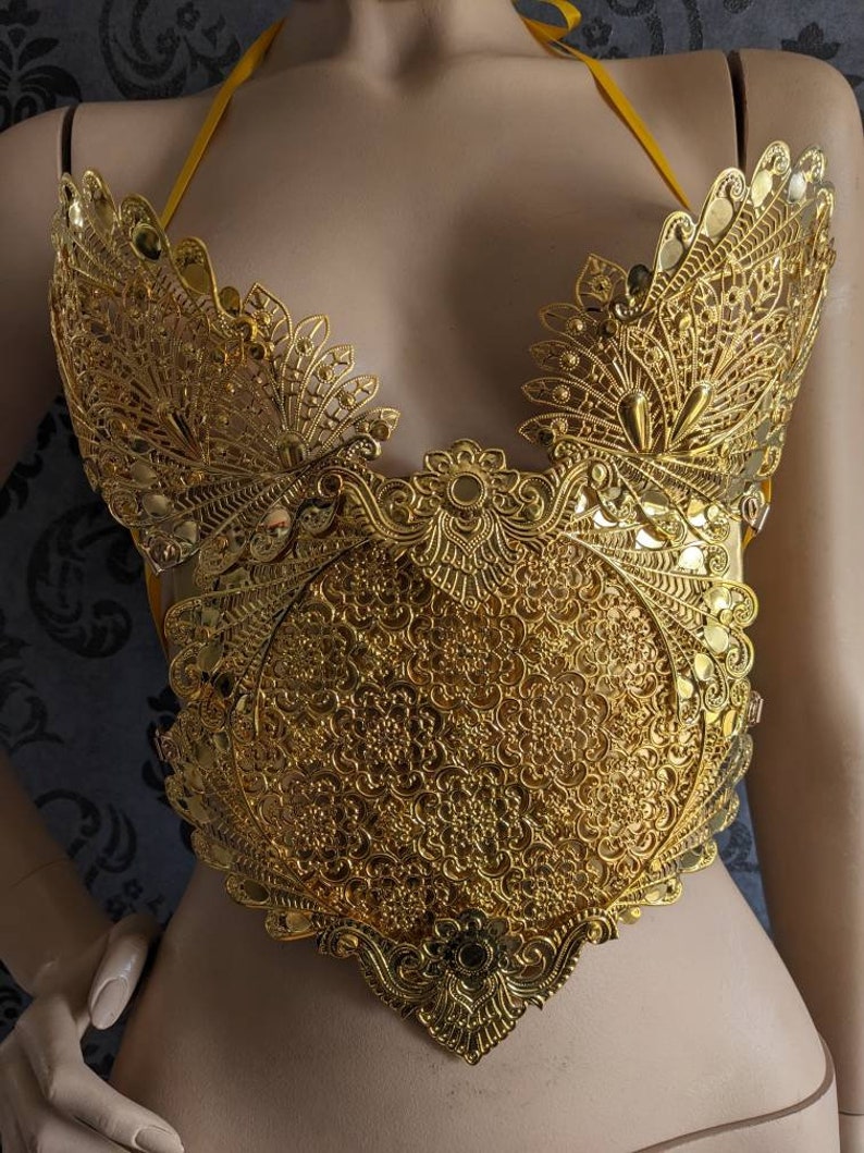May include: A gold-colored, ornate, decorative piece of jewelry with a delicate, intricate design. The piece is shaped like a heart and has a floral pattern.