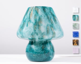 May include: A teal blue glass vase shaped like a mushroom with gold flecks throughout. The vase has a wide, rounded top and a smaller, round base.