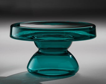 May include: Teal glass table with a round top and a wide, hourglass-shaped base.