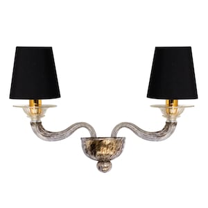 May include: A white and gold wall sconce with two black lampshades. The sconce has a curved design and a textured finish.