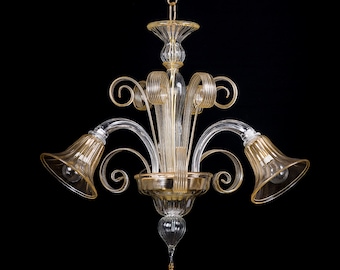 May include: A gold and clear glass chandelier with three lights. The chandelier has a traditional design with a central stem and three curved arms. Each arm has a bell-shaped glass shade.