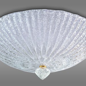 Puede incluir: Una lámpara de techo de cristal transparente con una superficie texturizada y ondulada. La lámpara tiene un centro dorado con un orbe de cristal transparente.