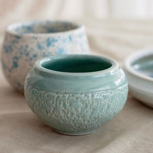 May include: A light blue ceramic bowl with a textured surface. The bowl is round and has a slightly flared rim.