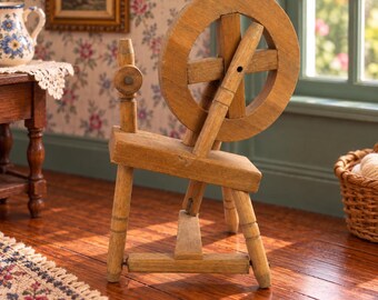 May include: A miniature wooden spinning wheel featuring a circular wheel, a vertical spindle, and a foot treadle. The structure is crafted from light brown wood with visible grain, standing on three legs with a horizontal base support.