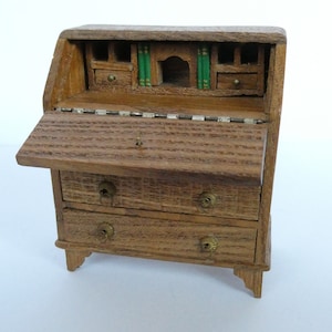 May include: A wooden miniature secretary desk with a drop-down front and three drawers. The desk has a small shelf with a decorative back and two small drawers above the larger drawers. The desk is painted in a natural wood finish.
