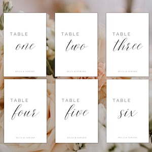 May include: Six white table number cards with black calligraphy. The cards are numbered one through six and have the text "Table" and "Bella & Edward" printed on them.