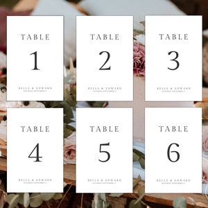May include: Six white table number cards with black text. The cards are numbered 1 through 6 and include the text "Table" and "Bella & Edward" with the wedding date.