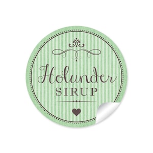 Könnte beinhalten: Ein runder Aufkleber mit grünen und weißen Streifen, einem braunen Wirbelmuster und dem Text "Holunder Sirup" in brauner Kursivschrift. Ein braunes Herz befindet sich in der Mitte des Aufklebers.