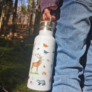 May include: White stainless steel water bottle with a wooden lid and a carrying handle. The bottle is decorated with a colorful illustration of woodland animals, including a deer, a badger, a squirrel, and a butterfly.