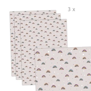 Könnte beinhalten: Eine Packung mit drei Bogen Geschenkpapier mit einem Regenbogen- und Tupfenmuster. Das Papier ist hellrosa mit kleinen weißen Punkten und einem sich wiederholenden Muster aus mehrfarbigen Regenbögen.