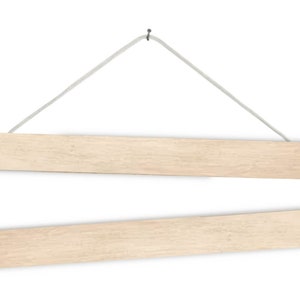 May include: A set of two wooden magnetic poster hangers, each measuring 51 inches long. The hangers are suspended from a white string and have a natural wood finish.