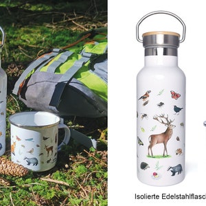 May include: A white insulated stainless steel water bottle and a white enamel mug with a forest animal design. The bottle has a bamboo lid and a carrying handle. The mug has a black rim and handle. The text "NEW!" is in the upper right corner of the image. The text "Isolierte Edelstahlflasche & Emaille Tasse" is at the bottom of the image.