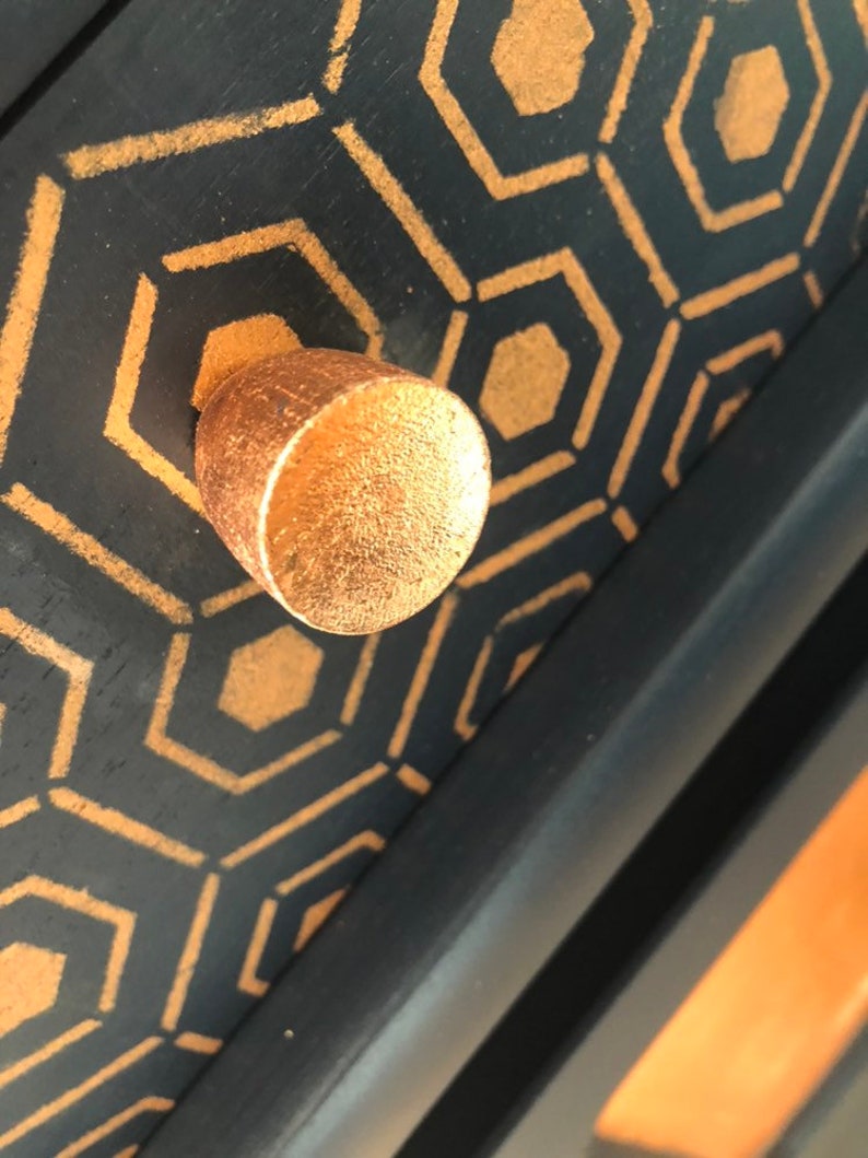 Puede incluir: Un pomo de caj&oacute;n de color dorado con una superficie texturizada sobre un fondo negro con un patr&oacute;n geom&eacute;trico de hex&aacute;gonos dorados.
