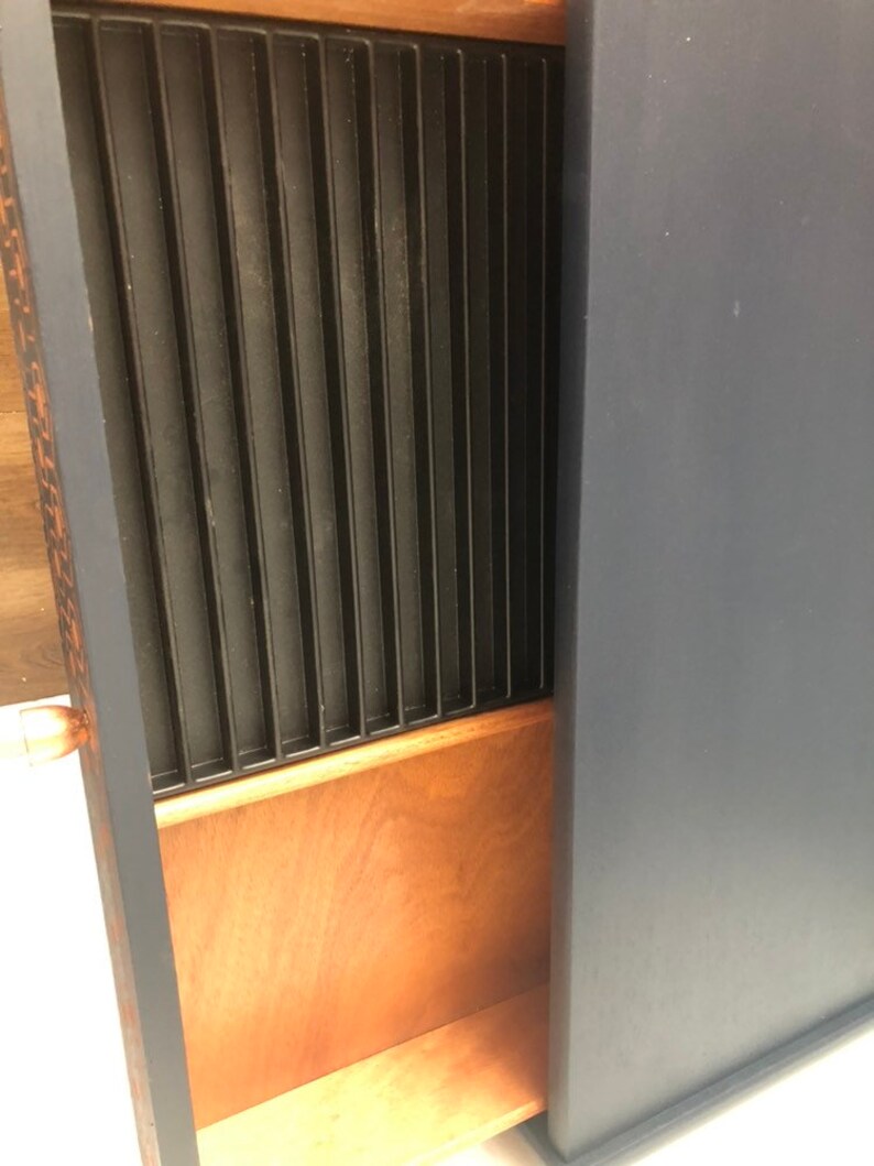 Puede incluir: Un armario azul oscuro con un caj&oacute;n de madera que tiene un divisor de metal negro en el interior. El caj&oacute;n est&aacute; abierto y el divisor es visible.