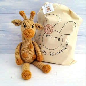 A yellow and gold crochet toy giraffe sat next to a Wee Woolly Wonderfuls crochet kit bag