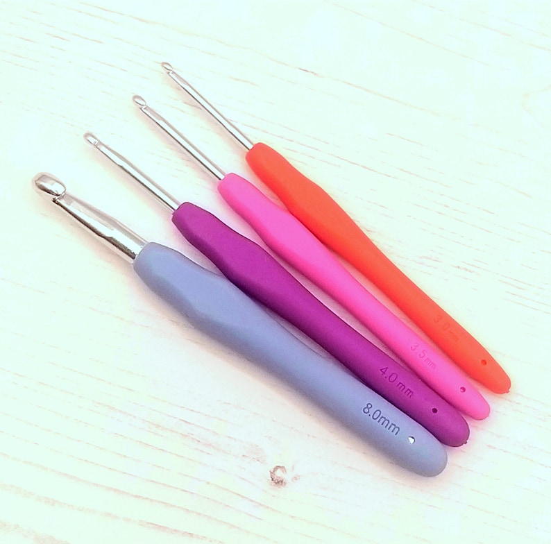 May include: Four crochet hooks in different sizes and colors. The hooks are 3.5mm, 4.0mm, and 8.0mm. The hooks are orange, pink, purple, and blue.