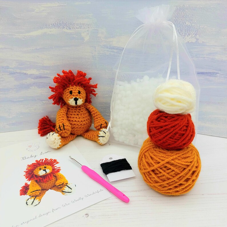 Puede incluir: Un kit de crochet para le&oacute;n con hilo naranja, rojo y blanco, relleno, un gancho de crochet e instrucciones. El kit incluye el texto "Baby Lion" y "un dise&ntilde;o original de Wee Woolly Wonderfuls".