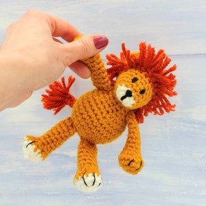 Puede incluir: Un juguete de le&oacute;n de crochet con pelo naranja y cuerpo marr&oacute;n. El le&oacute;n tiene ojos negros y nariz negra. El juguete est&aacute; siendo sostenido por una mano.