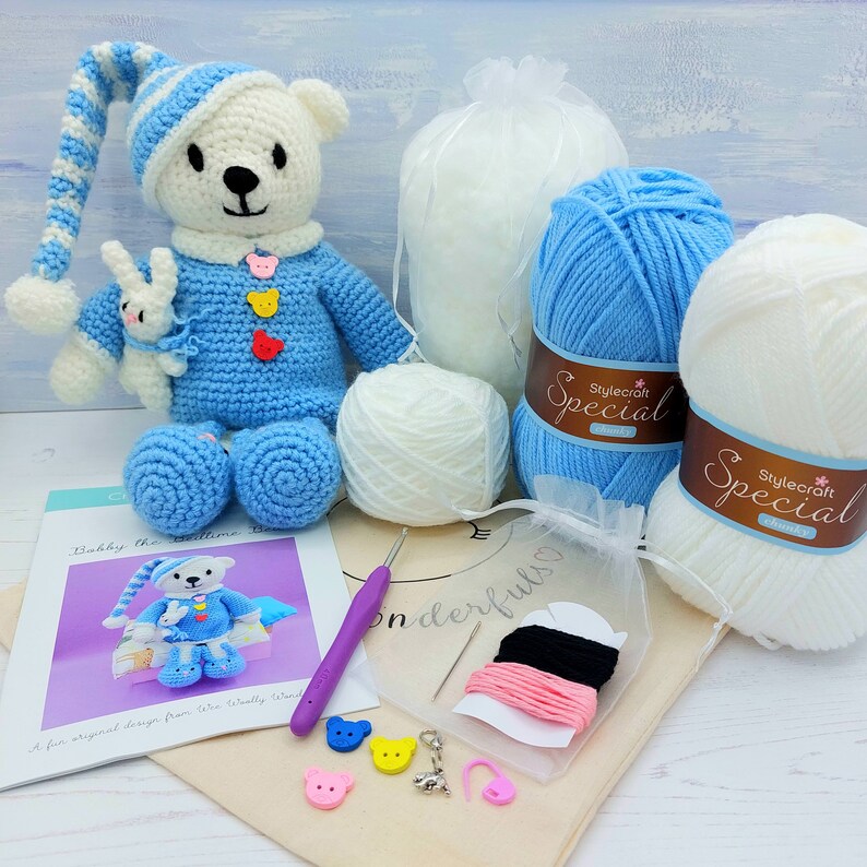 May include: A crochet kit featuring a white and blue bear doll wearing a matching nightcap and holding a small white rabbit. Includes two skeins of Stylecraft Special chunky yarn, a purple crochet hook, sewing needle, buttons, and a pattern.