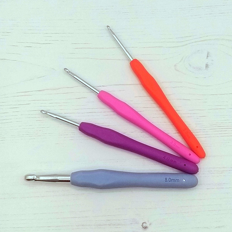 May include: Four crochet hooks in different colors and sizes. The hooks are orange, pink, purple, and gray. The sizes are 3.5 mm, 4.0 mm, and 8.0 mm.