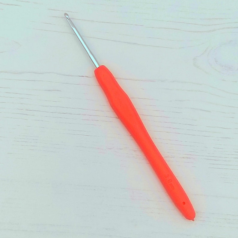 May include: A bright orange crochet hook with a silver hook. The hook is 5.00 mm.