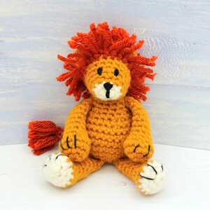Puede incluir: Un juguete de le&oacute;n de crochet con una melena naranja brillante, un cuerpo amarillo y patas blancas. El le&oacute;n tiene ojos negros y una nariz negra.
