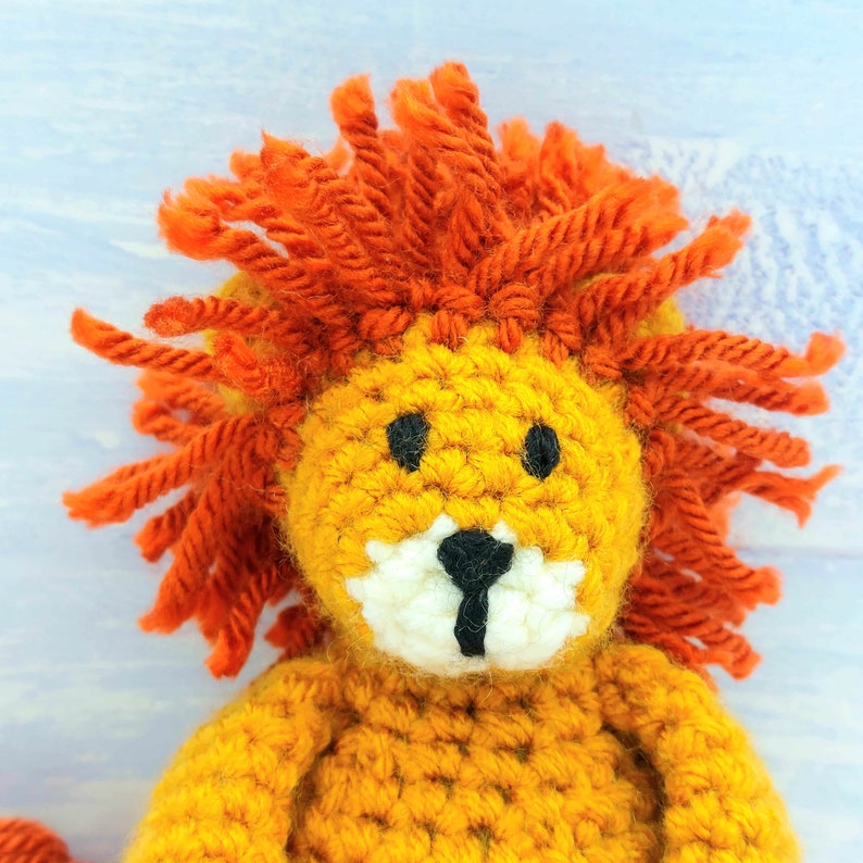 Puede incluir: Un juguete de le&oacute;n de crochet con pelo de lana naranja y un cuerpo de crochet amarillo. El le&oacute;n tiene ojos negros y una nariz negra.