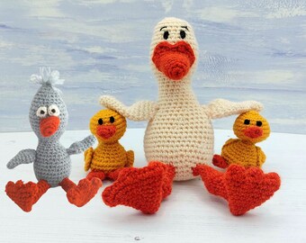 May include: A crocheted white goose with red feet and a red beak, surrounded by three crocheted ducklings. Two ducklings are yellow with orange beaks and feet, and one duckling is gray with an orange beak and feet.