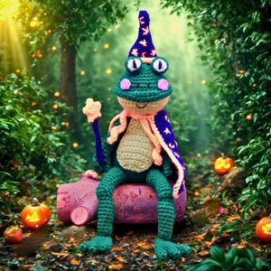 May include: A crocheted frog wizard with a blue and purple hat and cape, holding a star-shaped wand. The frog is green with pink accents and a beige belly, sitting on a pink log in a forest setting with pumpkins.
