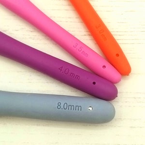 May include: Four silicone crochet hooks in different sizes and colors: orange (3.0 mm), pink (3.5 mm), purple (4.0 mm), and gray (8.0 mm).